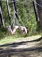 Submissive slut suspended helplessly from a tree